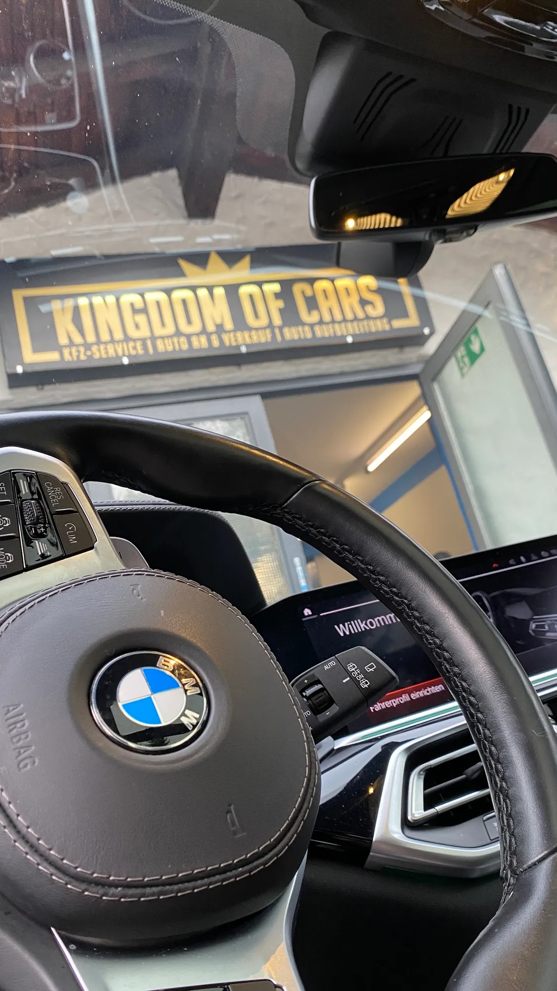 Cockpit eines BMW, durch die Windschutzscheibe ist das Kingdom-of-Cars-Schild zu sehen